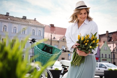 Beautiful woman with bouquet of yellow tulips and bicycle on city street