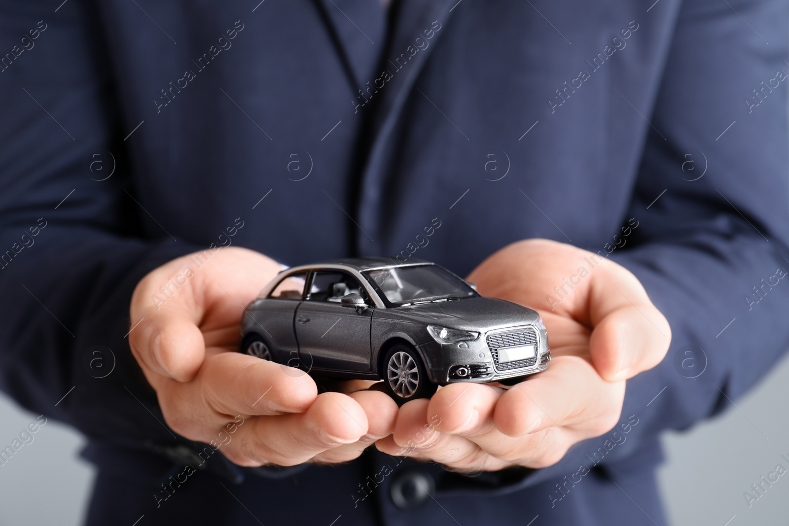 Photo of Male insurance agent holding toy car on grey background, closeup