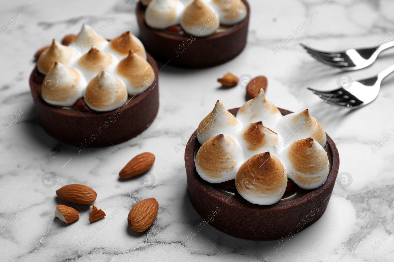Photo of Delicious salted caramel chocolate tarts with meringue and almonds on white marble table, closeup