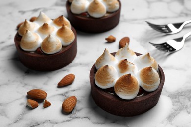 Photo of Delicious salted caramel chocolate tarts with meringue and almonds on white marble table, closeup