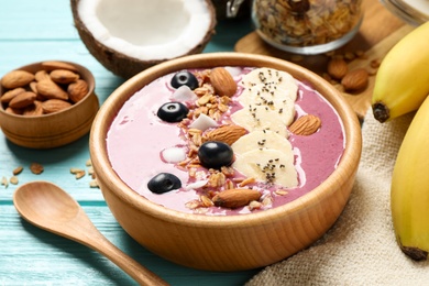 Photo of Delicious acai smoothie with granola and almonds served on light blue wooden table, closeup