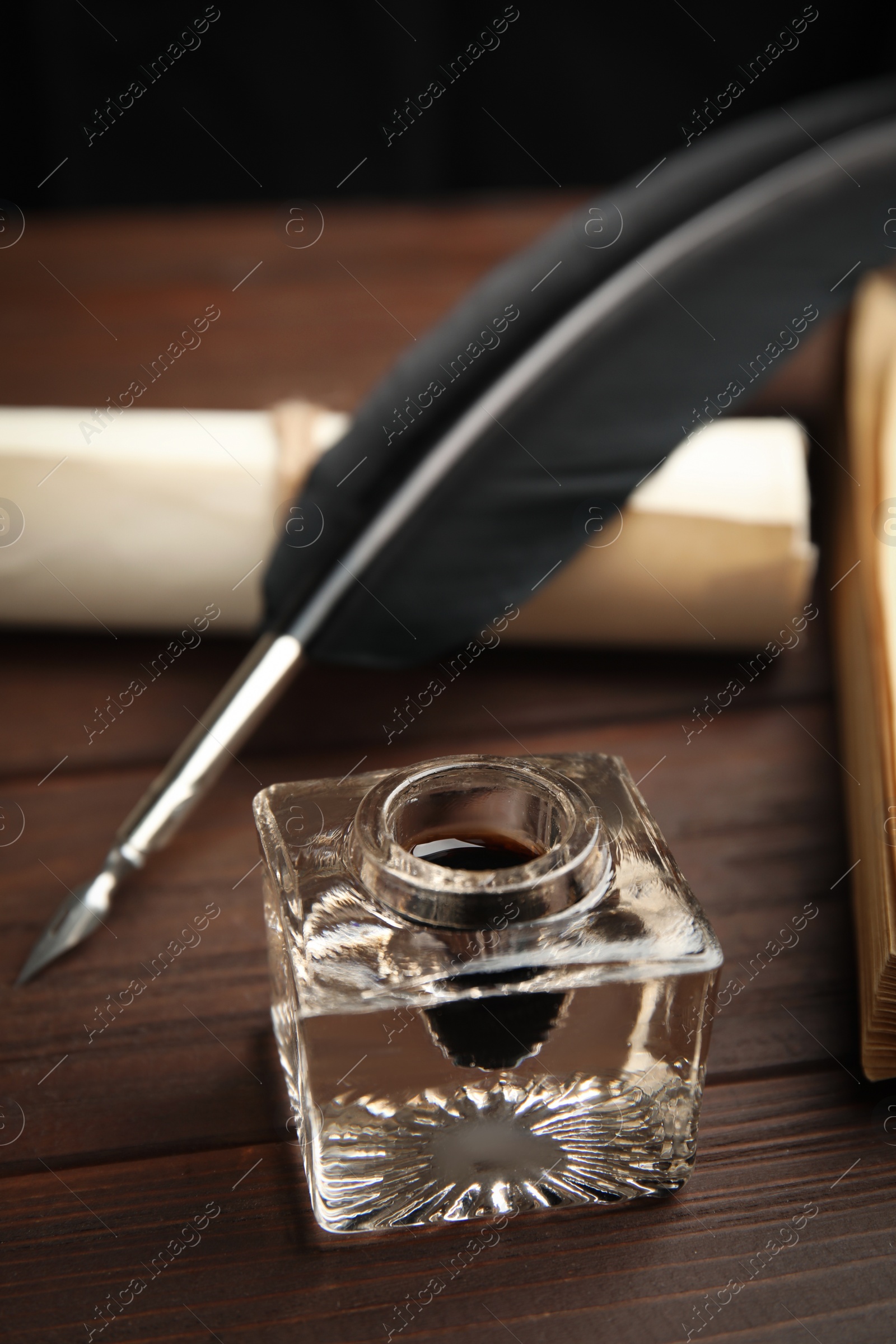 Photo of Feather pen, inkwell and paper roll on wooden table