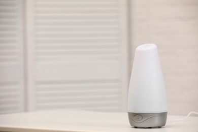 Photo of Modern essential oil diffuser on table indoors. Space for text