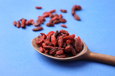 Photo of Dried goji berries in spoon on blue background, closeup