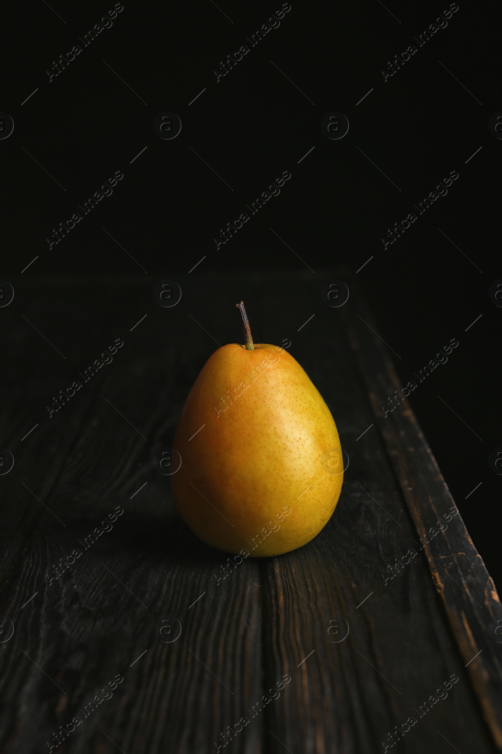 Photo of Ripe pear on wooden table against dark background