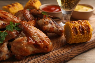 Delicious baked chicken wings, grilled corn and glass with beer on wooden table, closeup