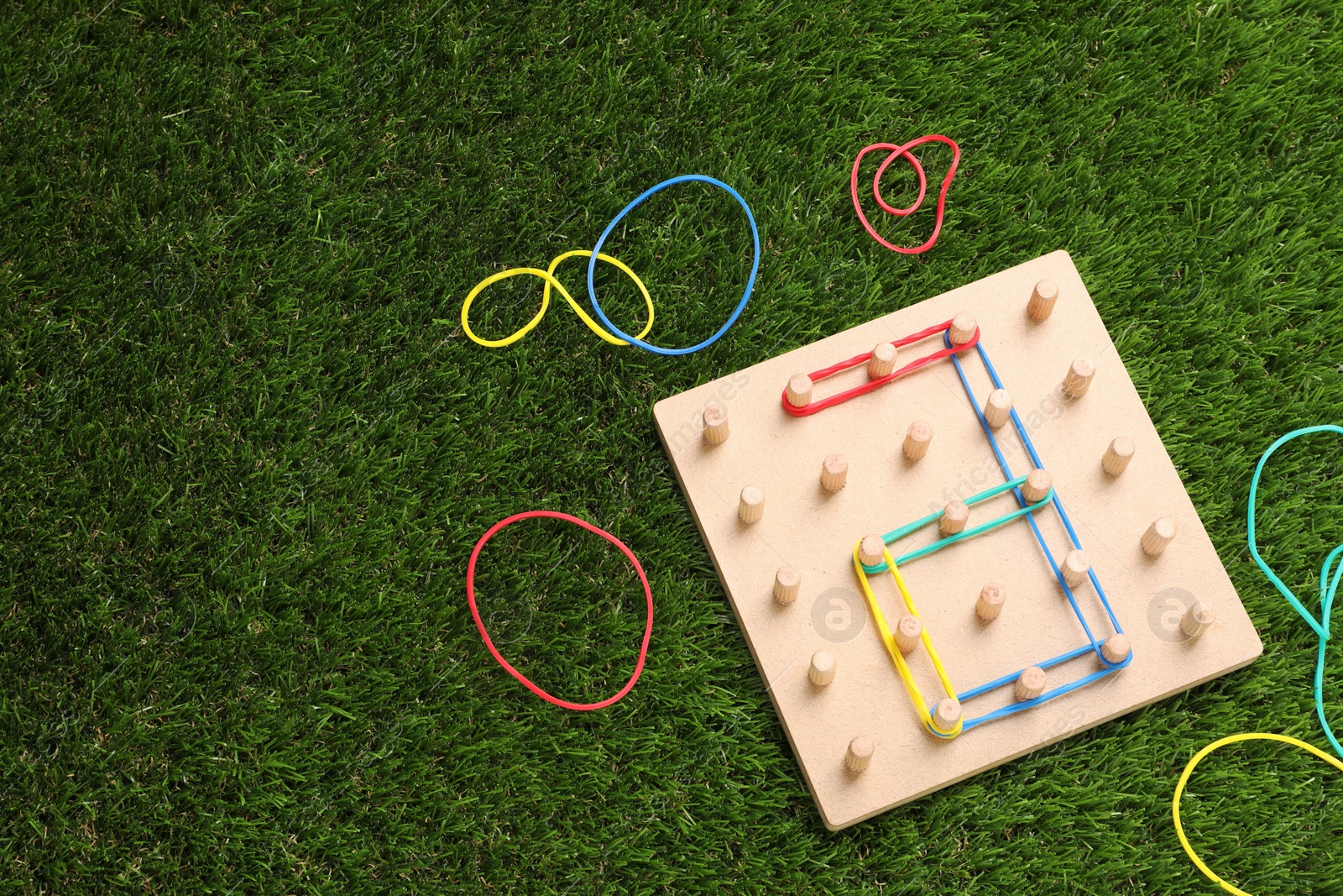 Photo of Wooden geoboard with number 6 made of rubber bands on artificial grass, flat lay and space for text. Educational toy for motor skills development