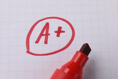 School grade. Red letter A with plus symbol on notebook paper and marker, top view