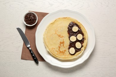 Photo of Stack of delicious crepes with chocolate and banana on white wooden table, flat lay