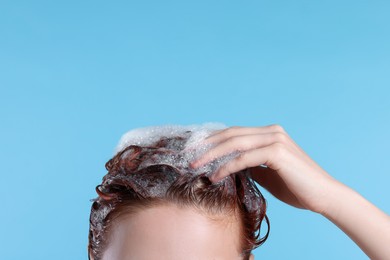Young woman washing her hair with shampoo on light blue background, closeup. Space for text