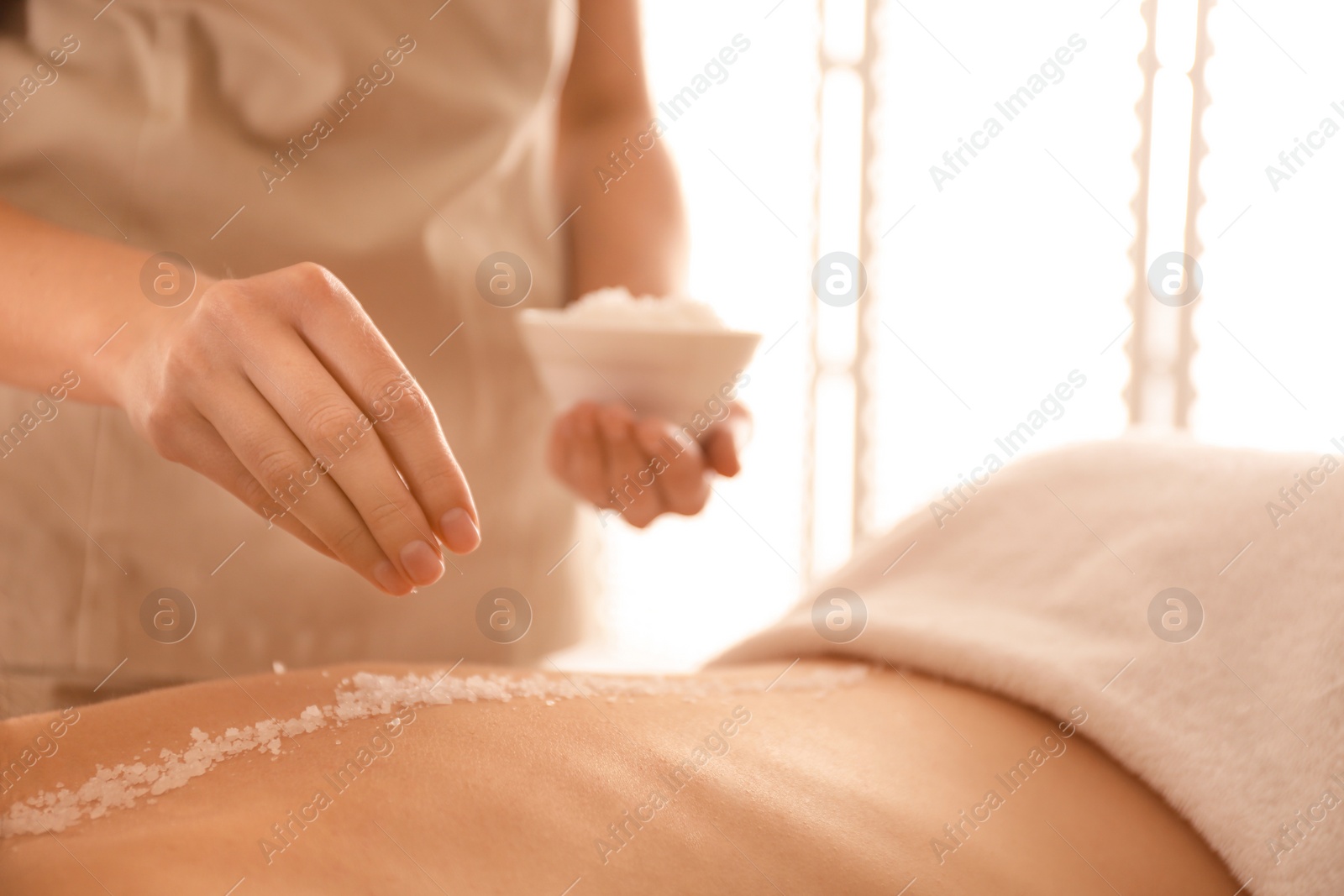 Photo of Young woman having body scrubbing procedure with sea salt in spa salon, closeup