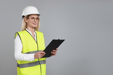 Photo of Engineer in hard hat holding clipboard on grey background, space for text