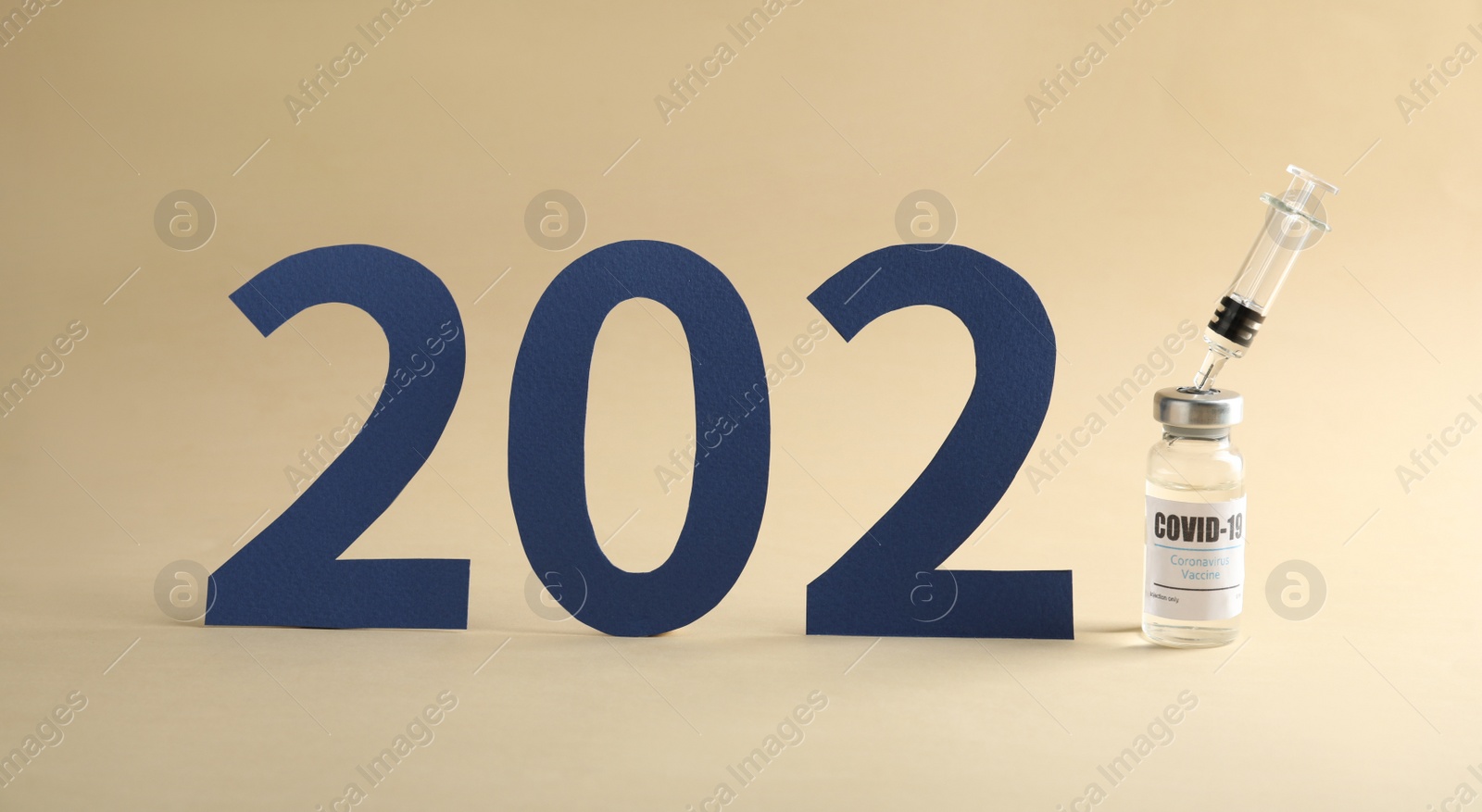 Photo of Paper numbers, syringe and vial with coronavirus vaccine forming 2021 on beige background