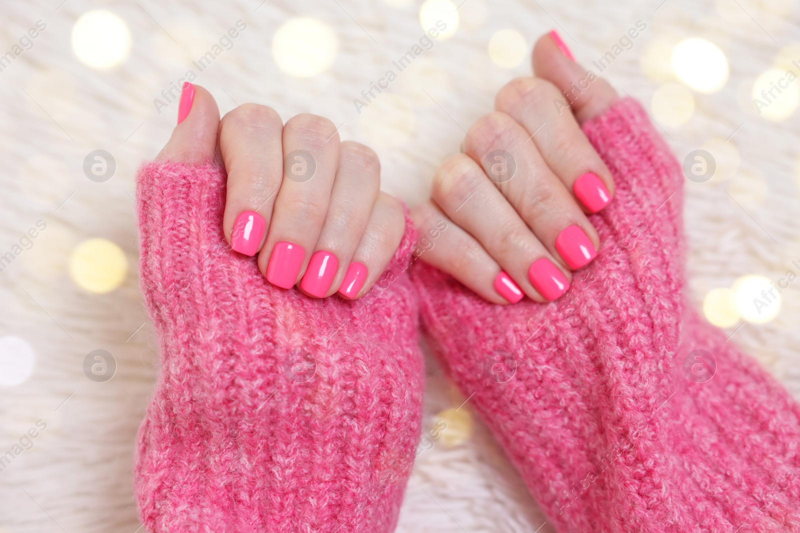 Photo of Woman showing her manicured hands with pink nail polish on faux fur mat, closeup. Bokeh effect