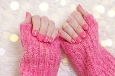 Photo of Woman showing her manicured hands with pink nail polish on faux fur mat, closeup. Bokeh effect