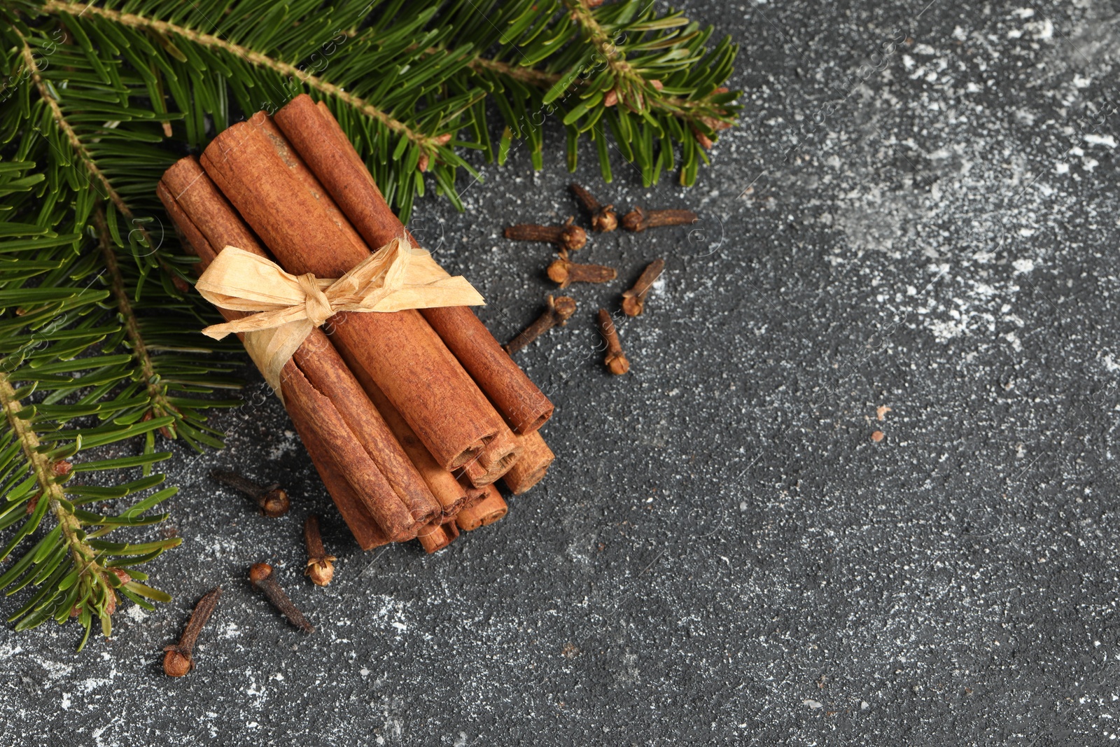 Photo of Different spices. Aromatic cinnamon sticks, clove seeds and fir branches on dark gray textured table, flat lay. Space for text