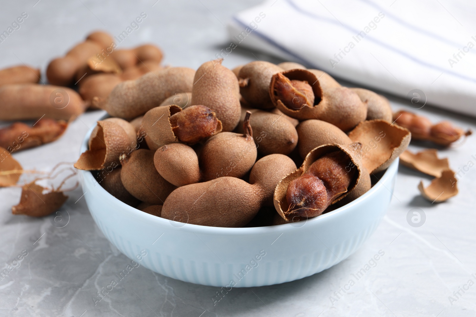 Photo of Delicious ripe tamarinds in ceramic bowl on light table