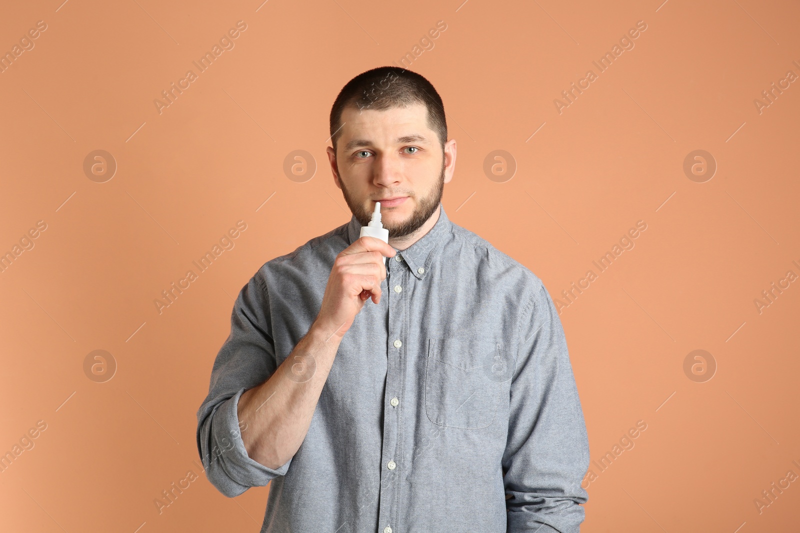 Photo of Sick man using nasal spray on orange background