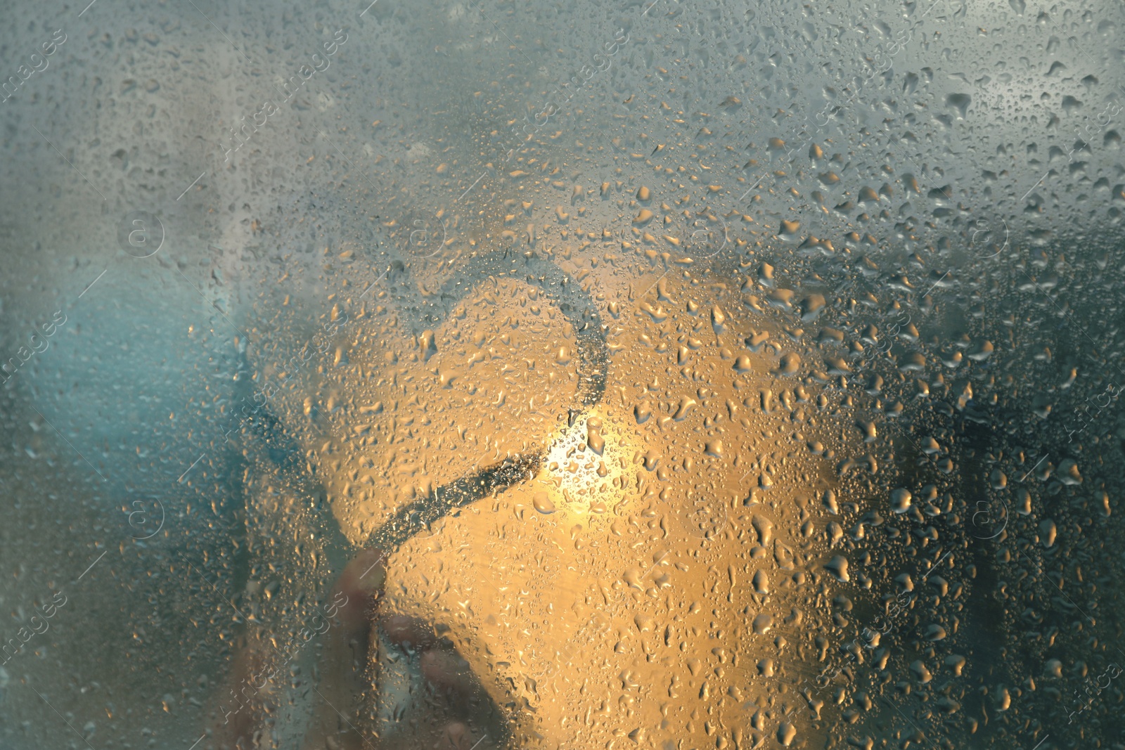 Photo of Woman drawing heart on foggy window at rainy weather, closeup