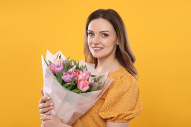 Happy young woman with bouquet of beautiful tulips on yellow background