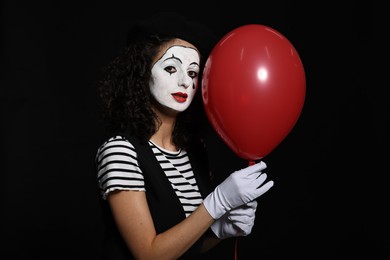 Photo of Young woman in mime costume with balloon posing on black background