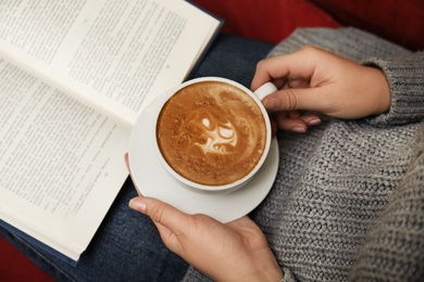 Photo of Woman with cup of coffee reading book at home, above view