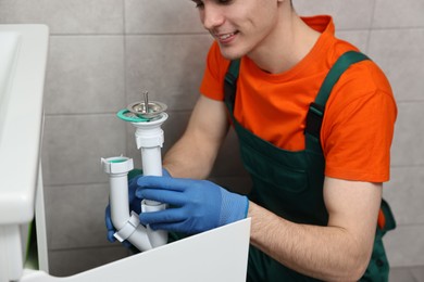 Photo of Smiling plumber wearing protective gloves repairing sink in bathroom, closeup