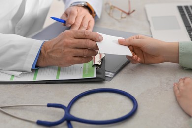 Photo of Doctor giving prescription to patient while filling medical card at table in clinic, closeup
