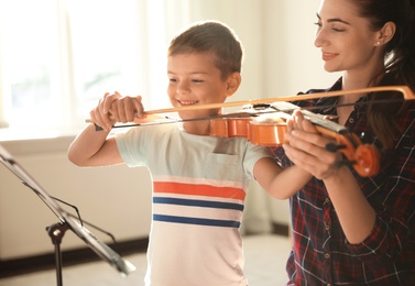 Young woman teaching little boy to play violin indoors