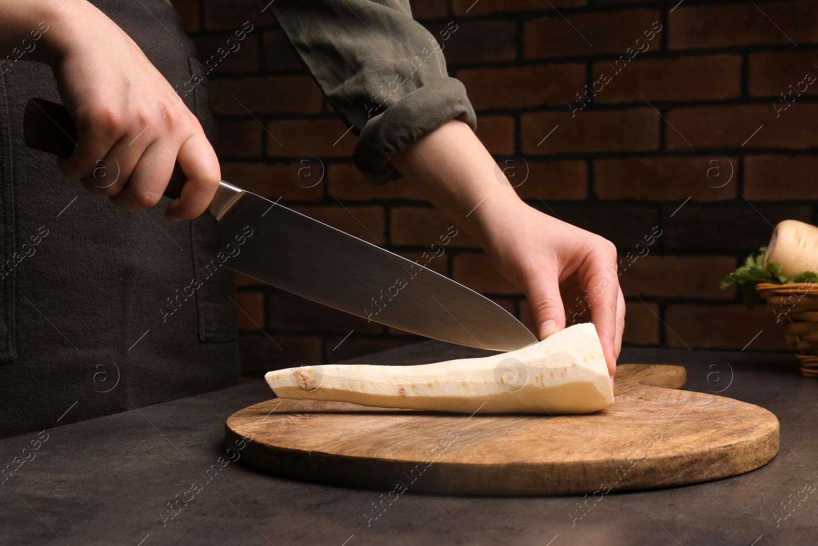 Photo of Woman cutting delicious fresh ripe parsnip at black table, closeup