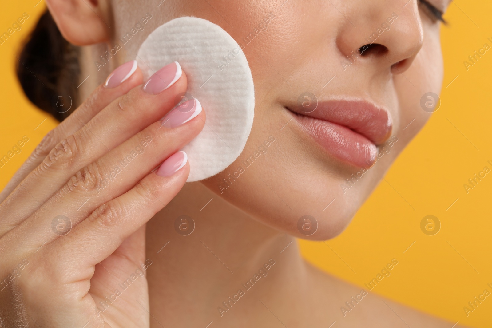 Photo of Beautiful woman removing makeup with cotton pad on orange background, closeup