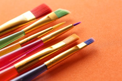 Photo of Set of different paintbrushes on orange background, closeup