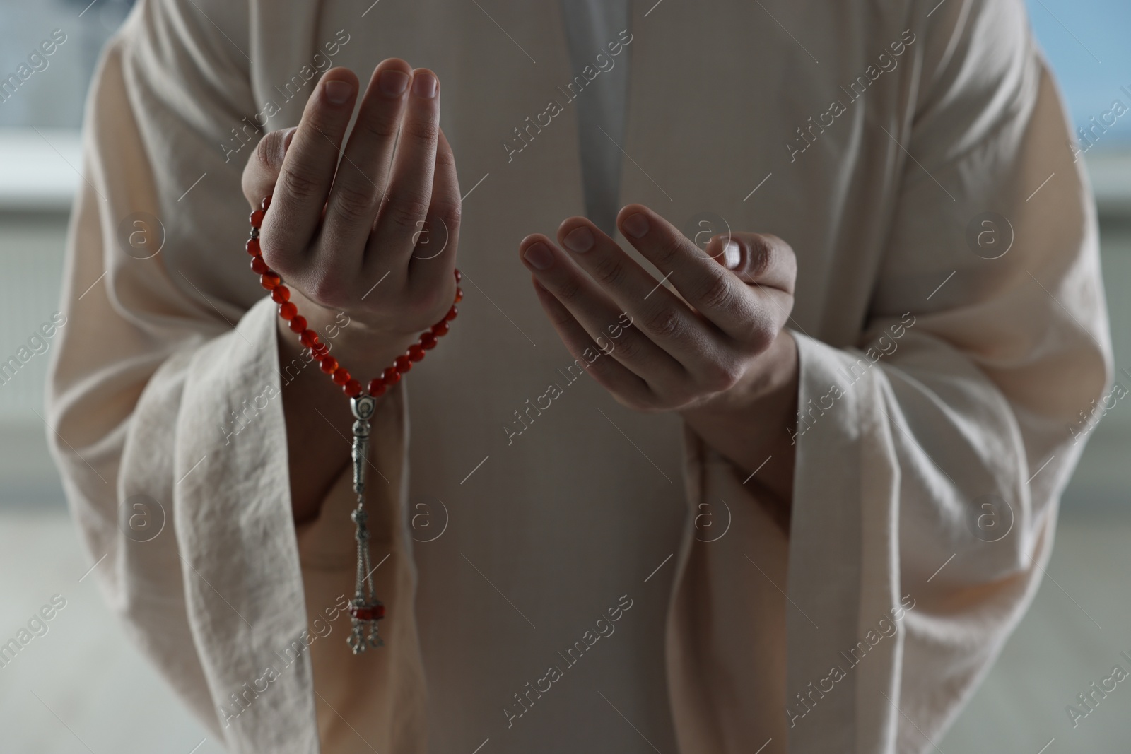 Photo of Muslim man with misbaha praying near window indoors, closeup
