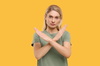 Photo of Stop gesture. Woman with crossed hands on yellow background