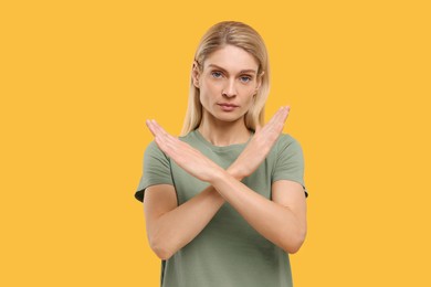 Stop gesture. Woman with crossed hands on yellow background