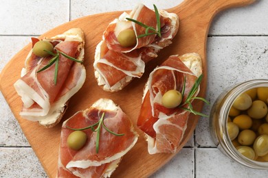 Photo of Tasty sandwiches with cured ham, rosemary and olives on tiled table, top view
