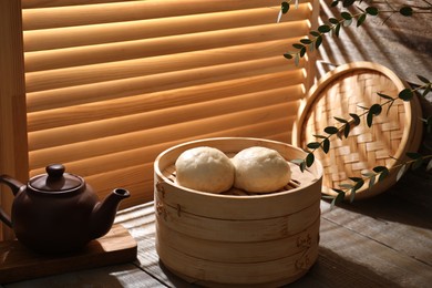 Delicious Chinese steamed buns and kettle on wooden table, closeup