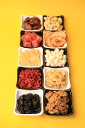 Photo of Bowls with dried fruits and nuts on yellow background