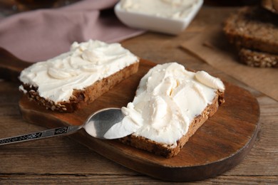 Photo of Bread with cream cheese on wooden table, closeup