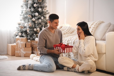 Photo of Boyfriend giving Christmas gift box to his girlfriend in living room