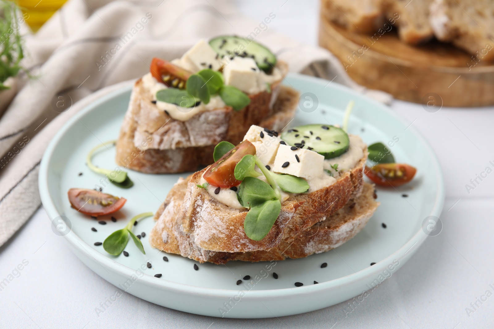 Photo of Tasty vegan sandwiches with tofu, cucumber, tomato and sesame seeds on white tiled table