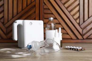 Photo of Modern nebulizer with face mask and medications on wooden table. Inhalation equipment