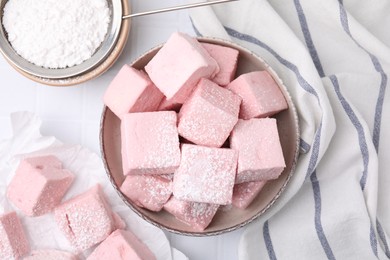 Bowl of delicious sweet marshmallows with powdered sugar on white table, flat lay