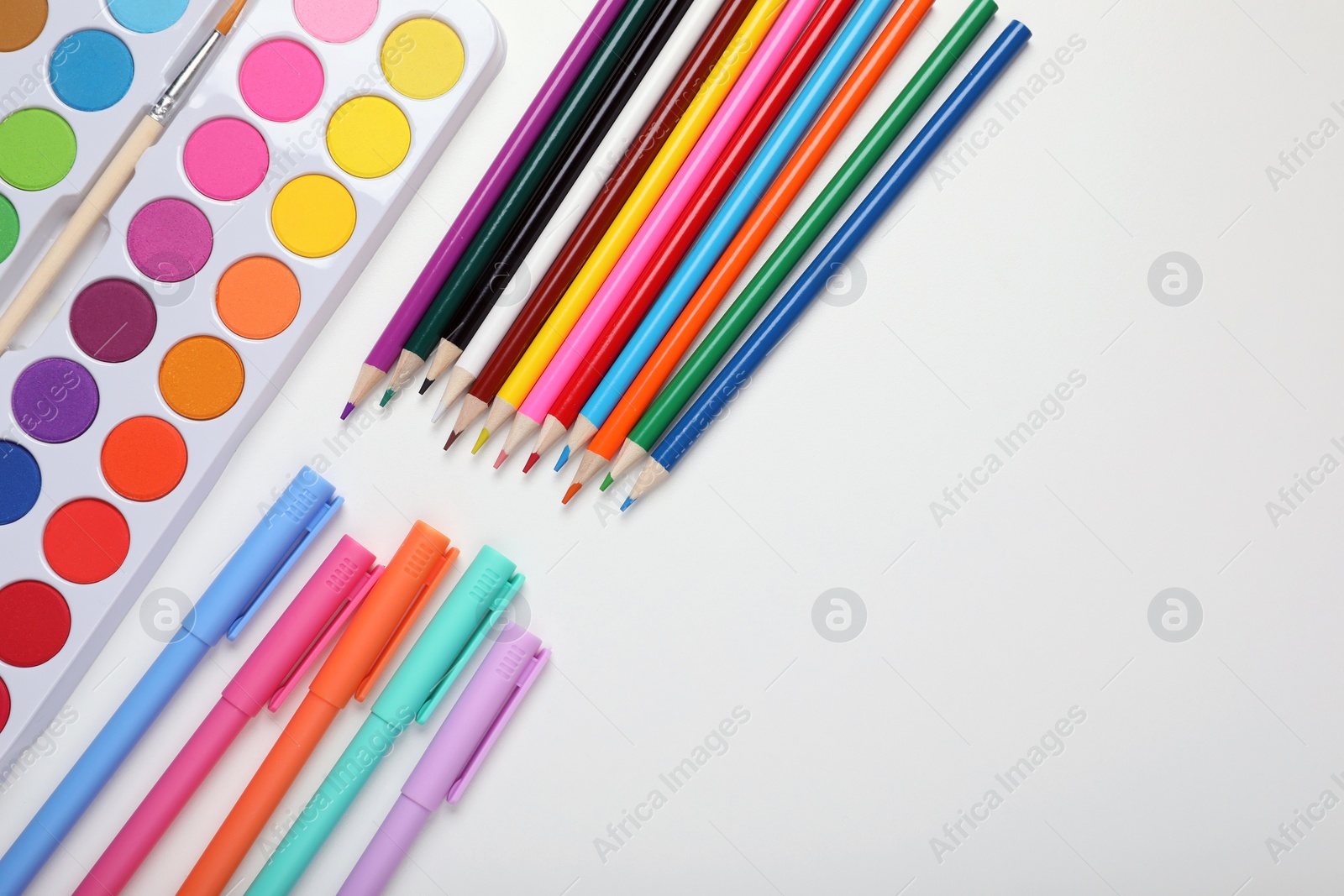 Photo of Watercolor palette, colorful pencils and markers on white background, flat lay. Space for text