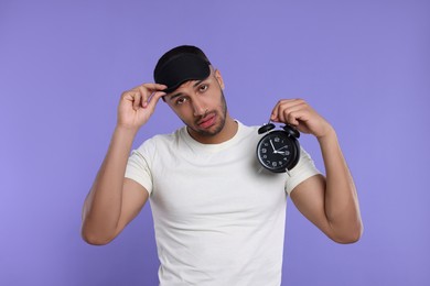 Tired man with alarm clock on violet background. Insomnia problem