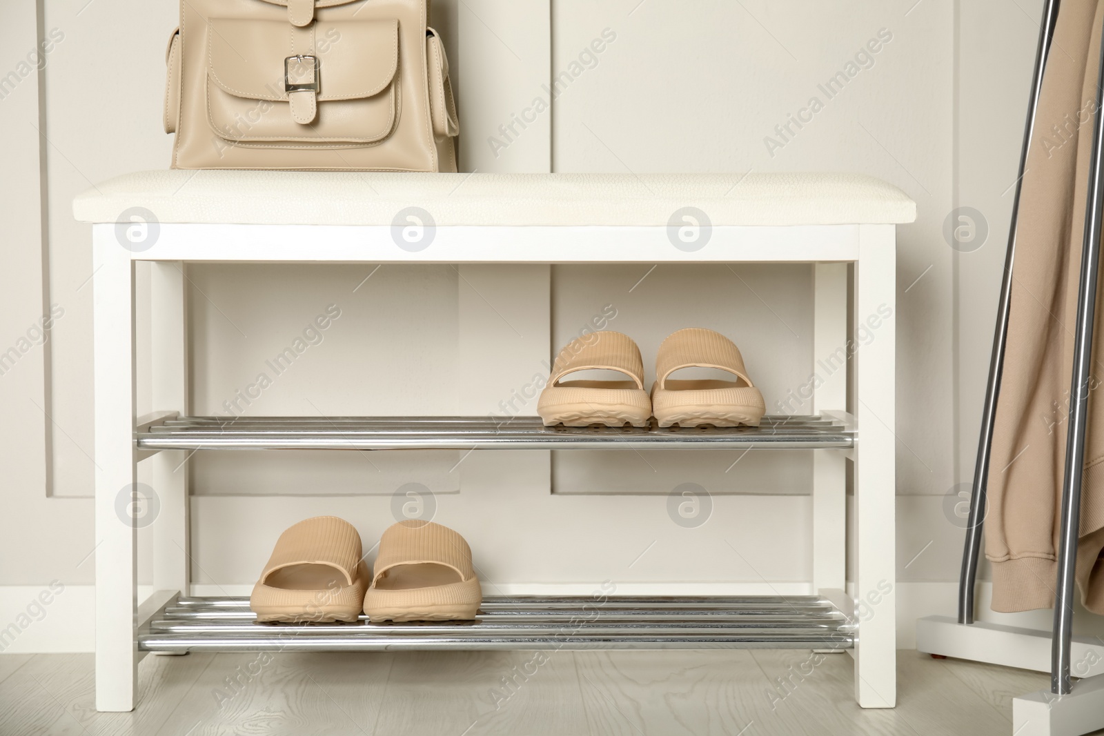 Photo of Storage bench with pairs of rubber slippers near white wall in room