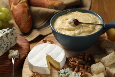 Photo of Fondue pot with tasty melted cheese, forks and different snacks on table