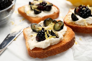 Photo of Tasty sandwiches with cream cheese, blueberries, blackberries and lemon zest on white table