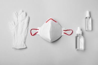Medical gloves, respiratory mask and hand sanitizers on grey background, flat lay