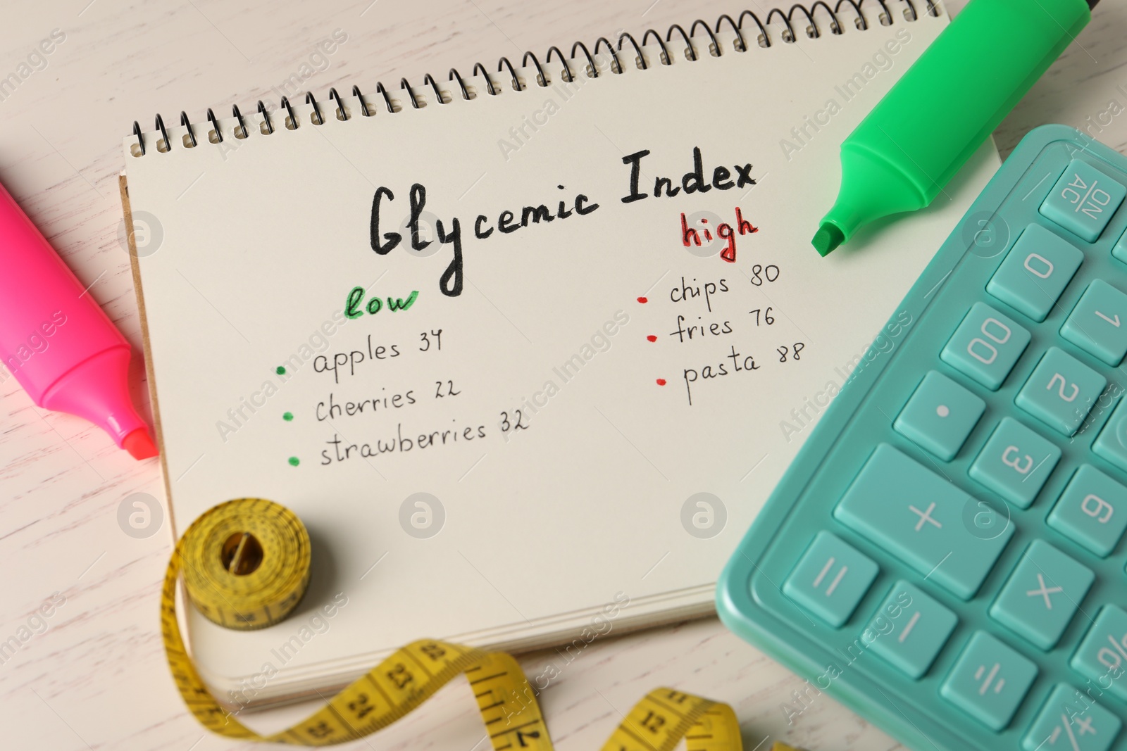 Photo of List with products of low and high glycemic index in notebook, markers, measuring tape and calculator on white wooden table, above view